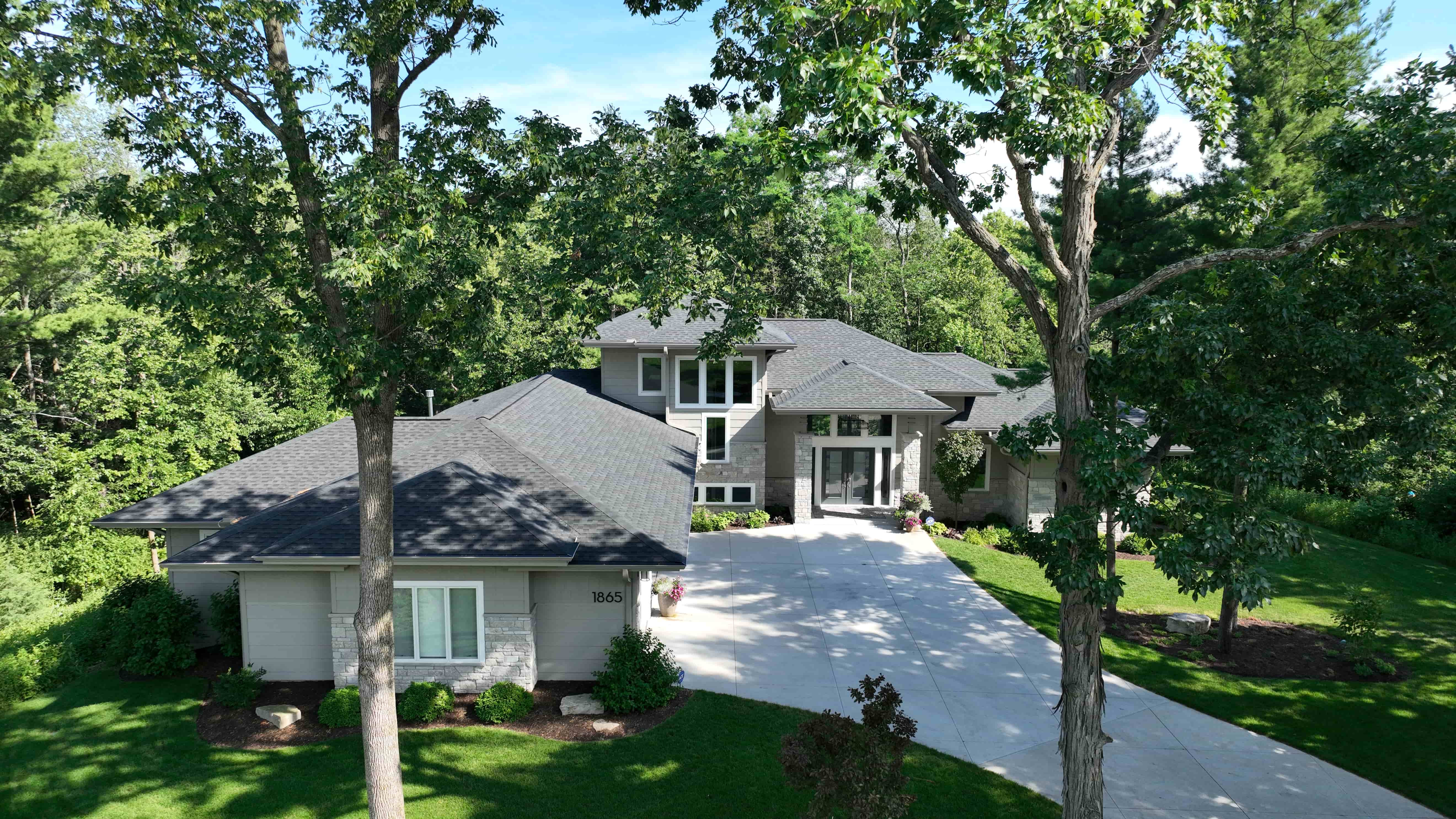 Modern suburban house with gray roof and stone accents surrounded by trees and a green lawn.
